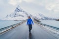 An Asian tourist man walking on road and traveling in Lofoten islands, Norway, Europe. White snowy mountain hills, nature Royalty Free Stock Photo