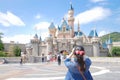 Asian tourist is taking a photo in front of a Disneyland castle in Hong Kong