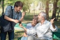 Asian tourists young man with smart mobile phone in his hands asks for directions from the old caucasian elder man who sit with Royalty Free Stock Photo