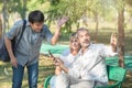 Asian tourists young man with smart mobile phone in his hands asks for directions from the old caucasian elder man who sit with Royalty Free Stock Photo