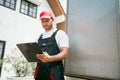 Asian truck driver wearing red cap holding a clipboard, checking the delivery packages checklists or paperwork and standing. Royalty Free Stock Photo