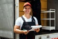 Asian truck driver wearing red cap holding a clipboard, checking the delivery packages checklists or paperwork and standing. Royalty Free Stock Photo