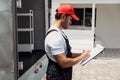 Asian truck driver wearing red cap holding a clipboard, checking the delivery packages checklists or paperwork and standing. Royalty Free Stock Photo