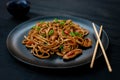 Asian udon noodles with chicken vegetables and teriyaki sauce with chopsticks on a black wooden background. Chinese and Japanese Royalty Free Stock Photo