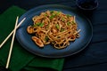 Asian udon noodles with chicken vegetables and teriyaki sauce with chopsticks and a green napkin on a black wooden background. Royalty Free Stock Photo