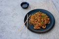 Asian udon noodles with chicken vegetables and teriyaki sauce with chopsticks and a linen napkin on a gray concrete background. Royalty Free Stock Photo