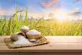 Asian uncooked white rice with the sunset rice field background and burlap sack on wooden table