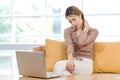 Asian upset suffered frowning face young female housewife sitting working with laptop on sofa couch in living room at home holding