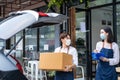 Asian waiter loads parcels into car with waitress check on clipboard. Cafe business owner couple wear mask, work in coffee shop