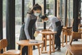 Asian waitress staff wearing protection face mask in apron cleaning table with disinfectant spray for protect infection coronaviru Royalty Free Stock Photo