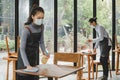 Asian waitress staff wearing protection face mask in apron cleaning table with disinfectant spray for protect infection coronaviru Royalty Free Stock Photo