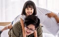 Asian warm family, father, daughter playing piggyback together in weekend on white bed in comfortable bedroom at home with love Royalty Free Stock Photo