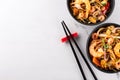 Asian wok noodles frying with prawns and mussels in a black bowl and chopsticks on a white marble background Royalty Free Stock Photo