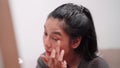 Asian woman applying eyeshadow in front of a large mirror after bathing and styling her hair at home.