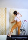 Asian woman applying new wallpaper at home. Renovate anddecoration