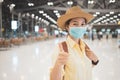 Asian woman backpacker wearing protective face mask giving thumbs up in an international airport