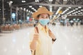 Asian woman backpacker wearing protective face mask giving thumbs up in an international airport