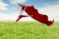 Asian woman ballerina holding red fabric making a big jump on blossom meadow. Royalty Free Stock Photo