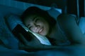 Asian woman on bed late at night texting using mobile phone tire Royalty Free Stock Photo