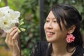 Asian woman in black dress holding and looking to white flower in leafy green garden.