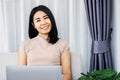 Happy Asian woman blogger sitting at sofa hand using laptop working from home