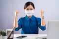 Asian woman in blue shirt wearing protective face mask showing her fist make a winning gesture and working at office.  on Royalty Free Stock Photo