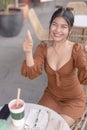 An Asian woman brightly beams for the camera holding a thumbs up as she finished writing down notes for her to-do-list