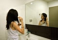 Asian Woman Brushing Hair In Front Of Mirror In Bathroom