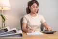 Asian woman calculating financial report with calculator, female businesswoman sign contract or writing documents paper at home Royalty Free Stock Photo