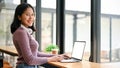 An Asian woman in casual clothes sits a table against the window with her laptop Royalty Free Stock Photo