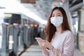 Asian woman in casual clothes wearing face mask using mobile phone while waiting for the train to go to work Royalty Free Stock Photo