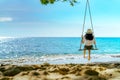 Asian woman in casual style wear hat swing the swings at sand beach and looking beautiful tropical paradise sea and sky on sunset Royalty Free Stock Photo