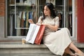 An Asian woman checked her purchased stuff in a shopping bag while resting on the stairs