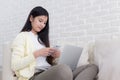 Asian women checking notification of mails on smartphone working with laptop computer on sofa