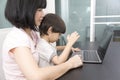 Asian woman with a child works on computer. Concept of work from home and home family education. Royalty Free Stock Photo