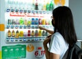 Asian woman choosing beverage on vending machine. Long hair woman wear black surgical mask selecting soft drink at modern beverage