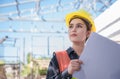 Asian woman civil engineer wear yellow safety hard hat standing and holding blueprint while checking infrastructure of building in