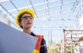 Asian woman civil engineer wears safety yellow helmet with goggles and holding blueprint while check to building in construction Royalty Free Stock Photo