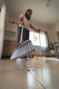 Asian woman cleaning and sweeping dust the floor with a broom in the living room. Woman doing chores at home. Royalty Free Stock Photo