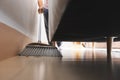 Asian woman cleaning and sweeping dust the floor under the sofa with a broom in the living room. Royalty Free Stock Photo