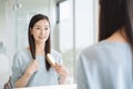 Asian woman combing hair in front of mirror.