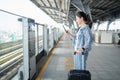 Asian woman commuter standing on the subway platform waiting to go inside train. She is using a smart phone with a suitcase Royalty Free Stock Photo