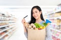 Asian woman with credit card holding paper bag full of groceries isolated on studio white background Royalty Free Stock Photo