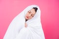 Asian woman curled up in blankets on pink background Royalty Free Stock Photo