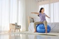 Asian woman doing yoga exercise with fitness ball in her bedroom as a result of social distancing and quarantine period Royalty Free Stock Photo