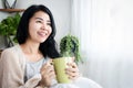 Beautiful Asian woman drinking coffee at home in the morning sitting in bed next to the window, smiling and relaxing Royalty Free Stock Photo