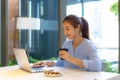 Asian woman drinking coffee in mug and smiling happily while taking a break from work at her computer during work at home in the Royalty Free Stock Photo