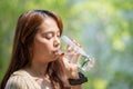 Asian Woman drinks water from tall glass of water at outdoor tree bokeh green background Royalty Free Stock Photo