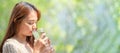 Asian Woman drinks water from tall glass of water at outdoor tree bokeh green for banner background Royalty Free Stock Photo
