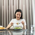 Asian woman eating vegetable salad mix with tomato for healthy meal on the table in dining room at home Royalty Free Stock Photo